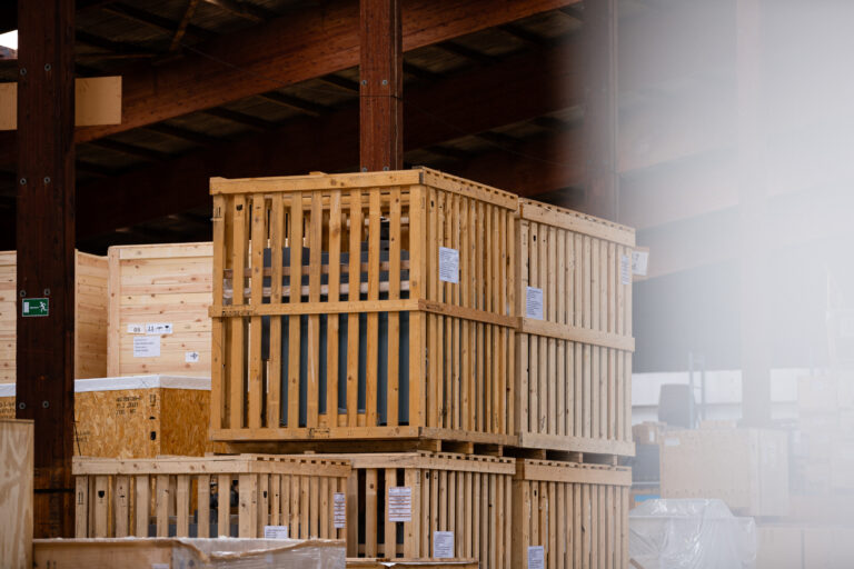 Transportkisten, unter anderem aus Holzpaletten, sind in einer Lagerhalle gestapelt.