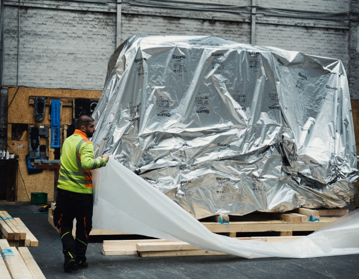 Ein Mann in Warn-Kleidung verpackt Ware mit Folie als Industrieverpackung.